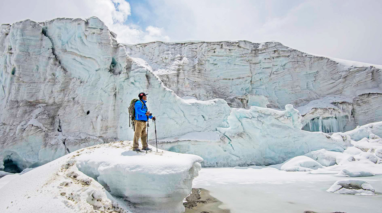 Lone hiker on snow-covered Qelqaya glacier with bright blue jacket against icy formations, showcasing Cuzco's new travel d...